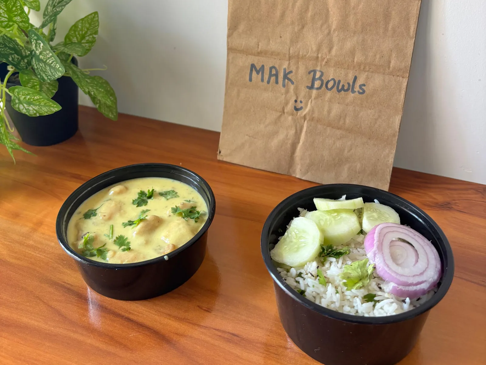 Kadhi with pakoras, garnished with coriander, next to a bowl of jeera rice with cucumber slices and onion.