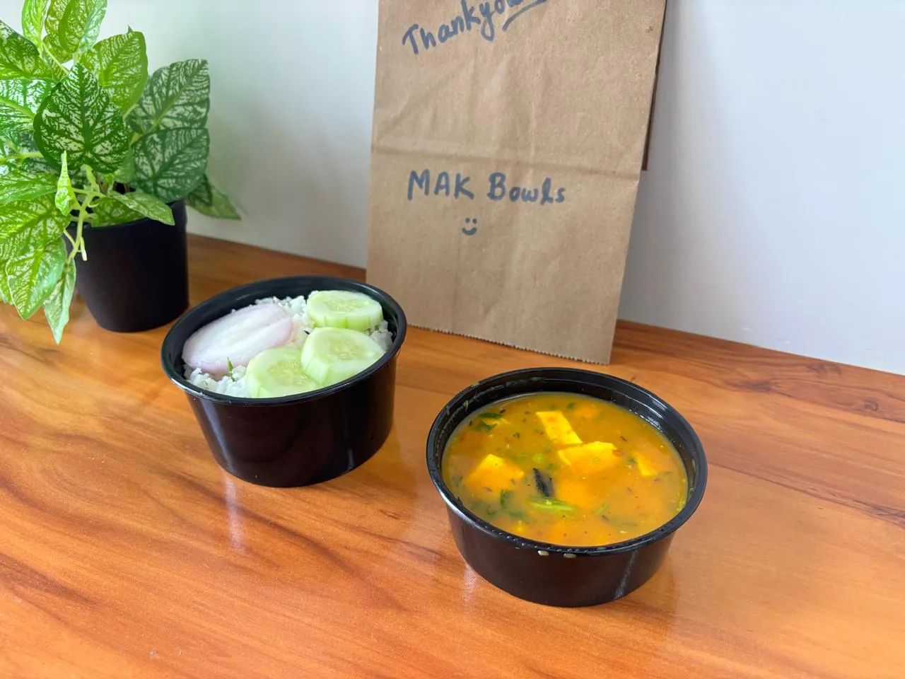 A paneer curry with spinach next to a bowl of jeera rice with cucumber slices and onion.