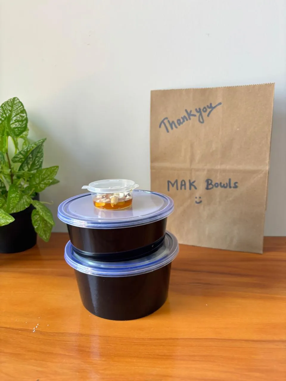 Two lidded MAK Bowls meal containers stacked with a small side cup on top, in front of a paper bag marked MAK Bowls.